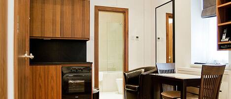 Una cocina compacta con gabinetes de madera y un horno empotrado, un área de comedor con mesa y sillas, y un espejo grande en la pared.