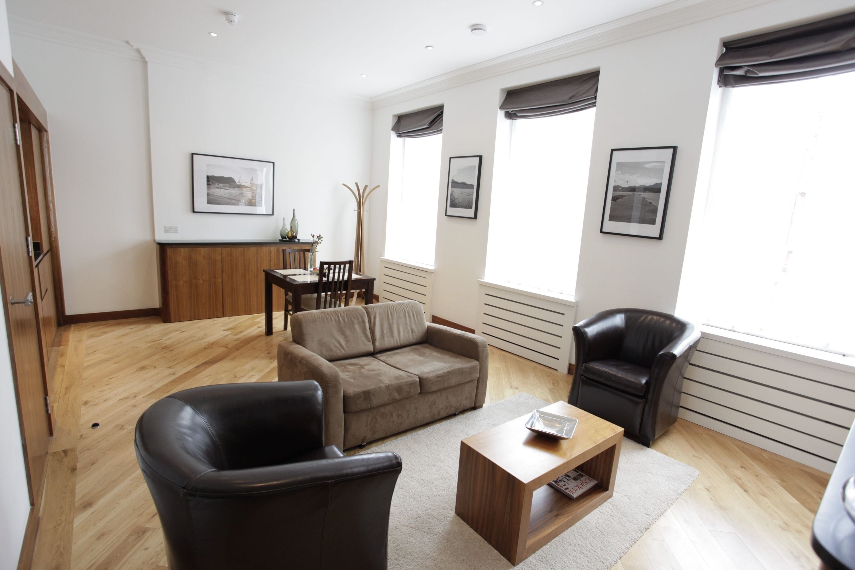 A modern living room with a sofa, two armchairs, a coffee table, and a dining area with a table and chairs.