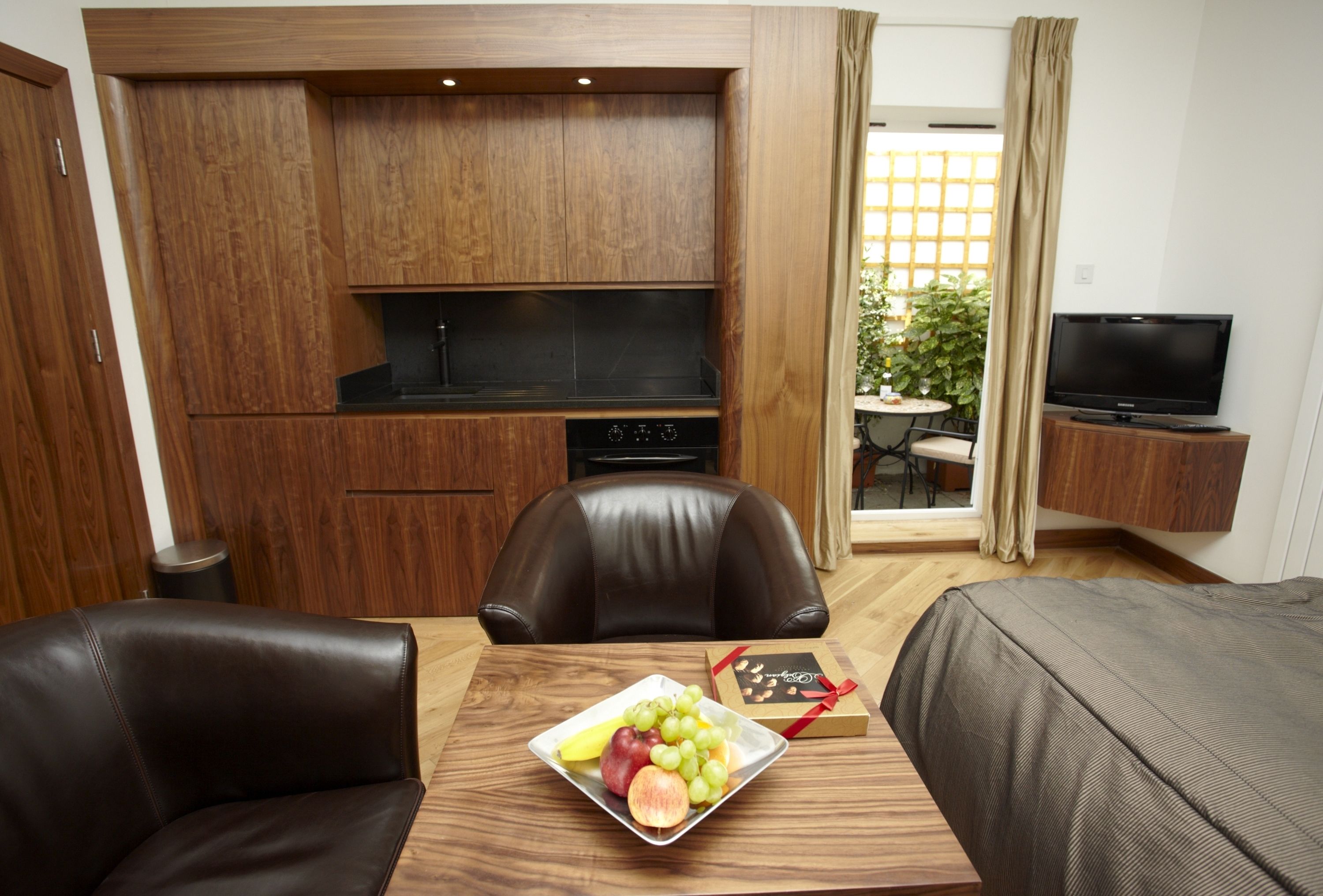 A compact hotel room with a kitchenette, a dining area with a table and chairs, a sofa, and a television.