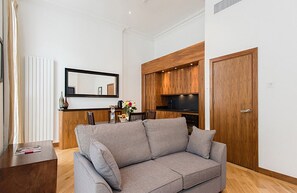 Ein modernes Wohnzimmer mit grauem Sofa, Holzschränken, einer Küchenzeile und einem großen Spiegel.