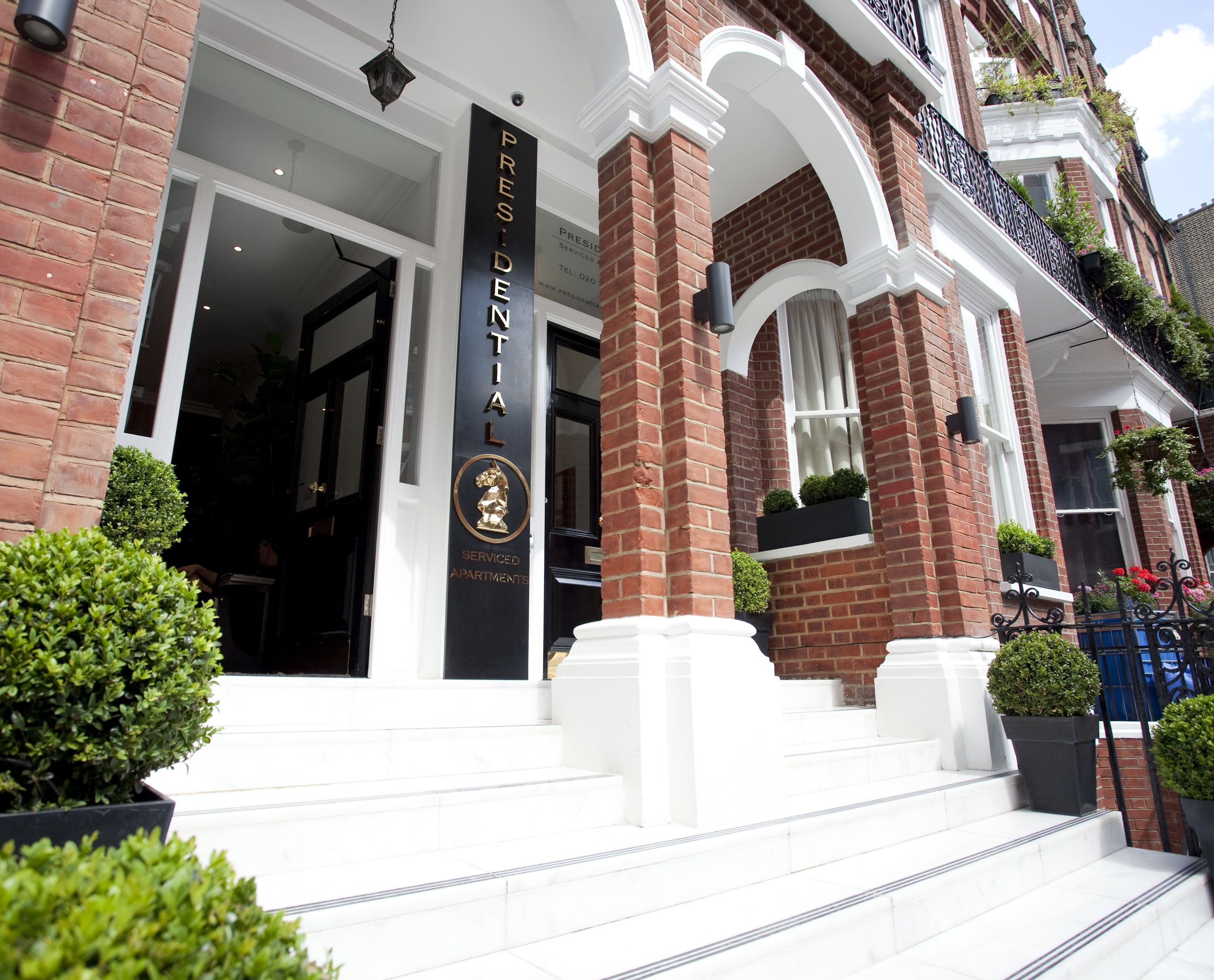 A building entrance with a sign reading "President Apartments" and a logo. There are steps leading up to the entrance, and the building has brick walls and white trim.