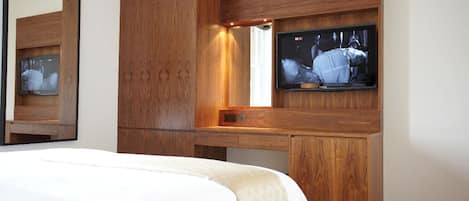 Habitación de hotel con una cama grande, un armario de madera, un televisor montado en la pared y un espejo que refleja parte de la habitación.