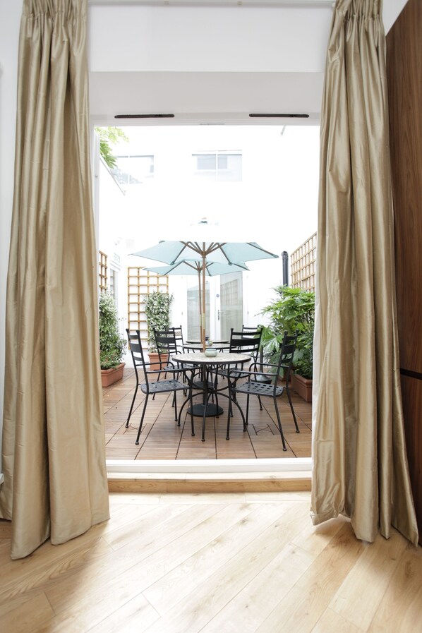 An open patio with a table and chairs, a green umbrella, and potted plants.
