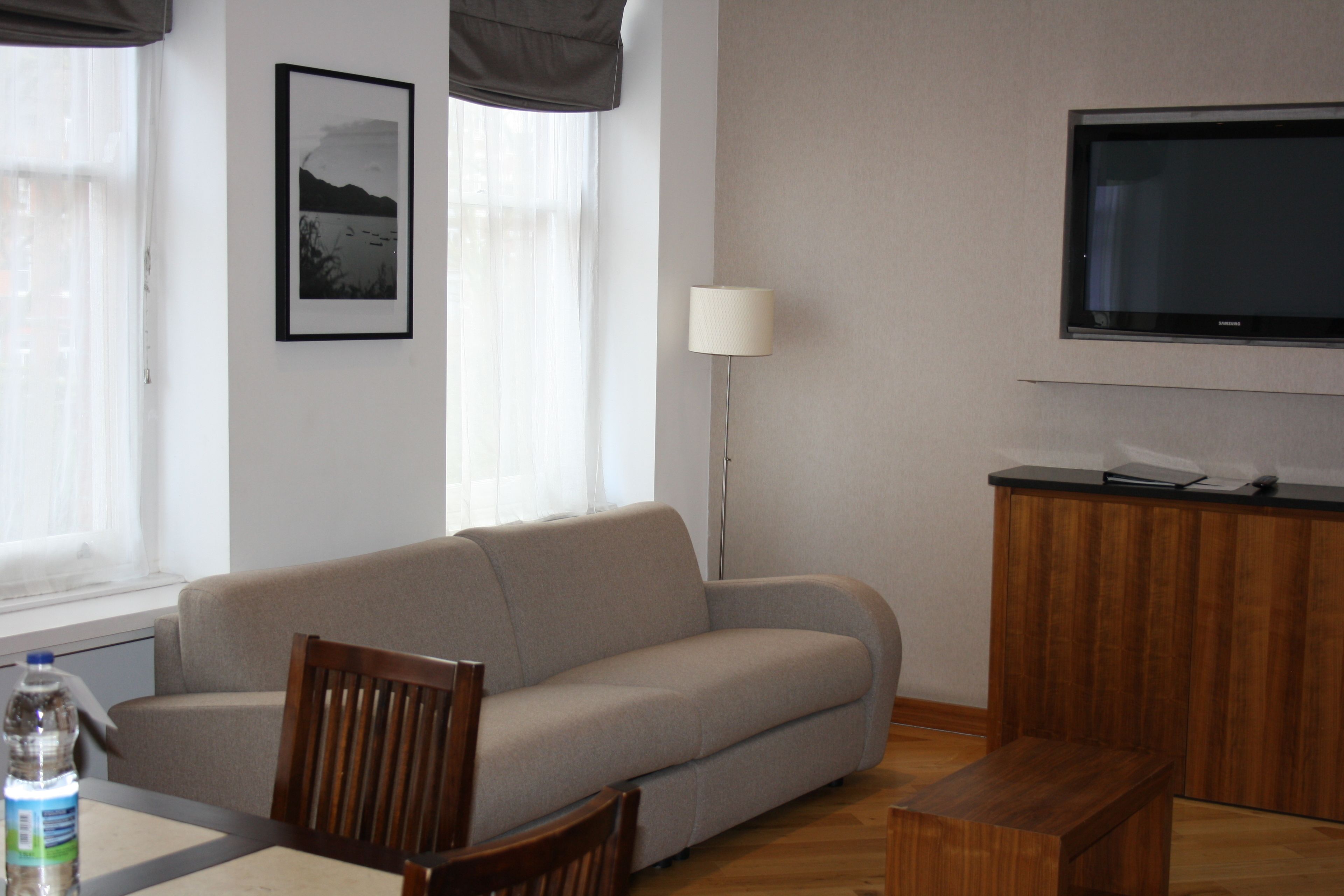 A living room with a sofa, a wooden coffee table, a TV mounted on the wall, a lamp, and a framed picture on the wall.