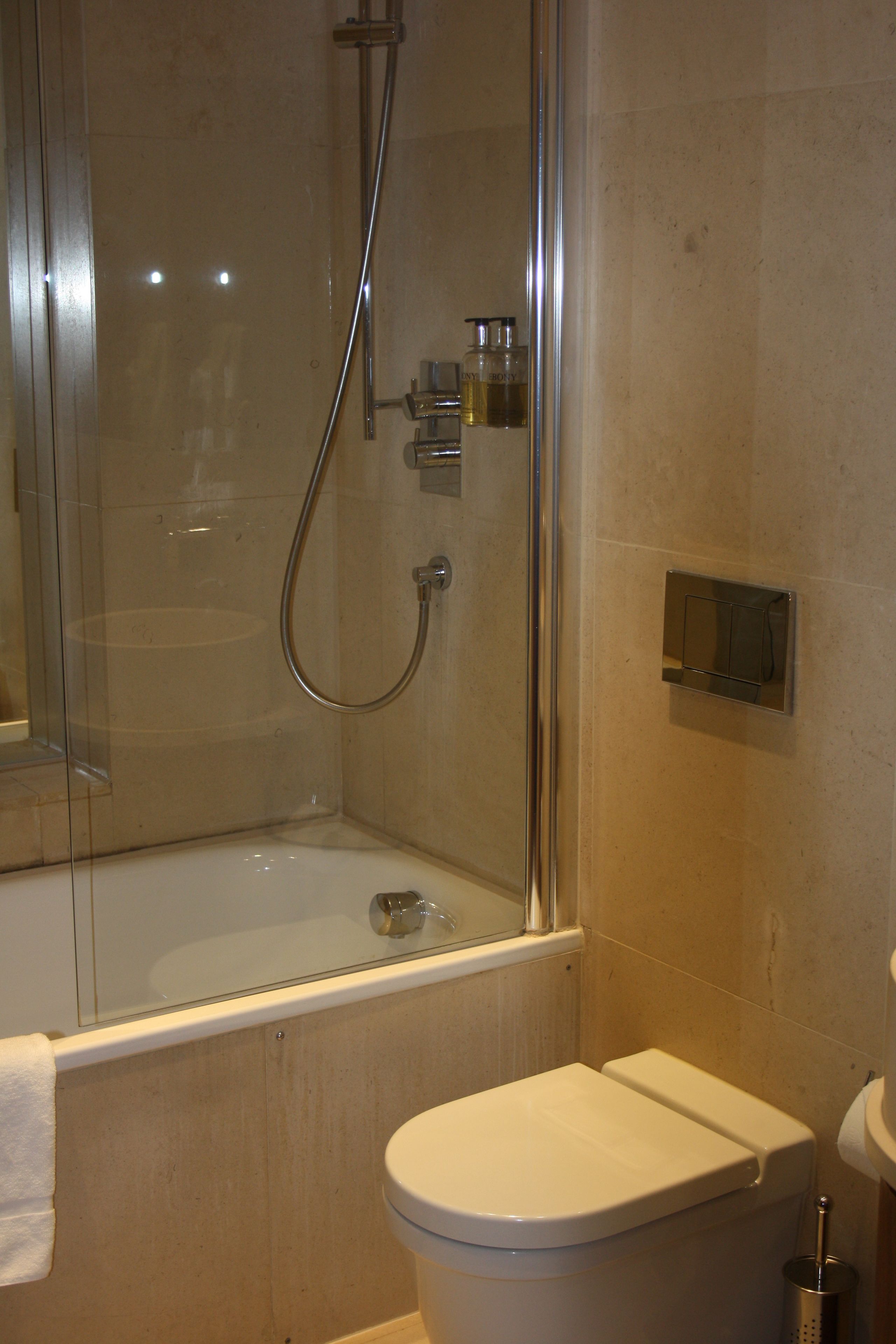 Een moderne badkamer met een glazen douchecabine, een witte badkuip en een toilet.