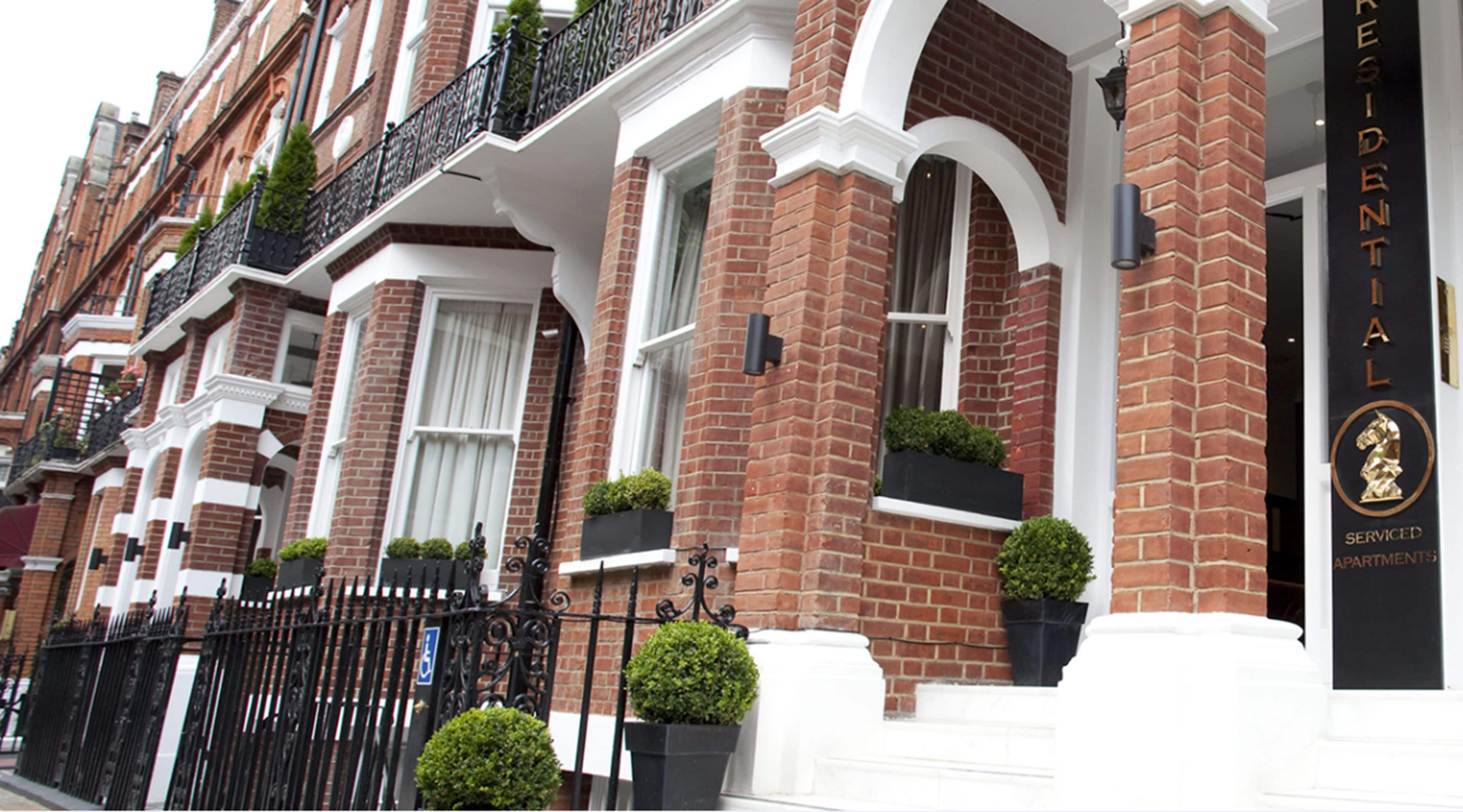 A row of red brick townhouses with white trim, black wrought iron balconies, and small potted plants.