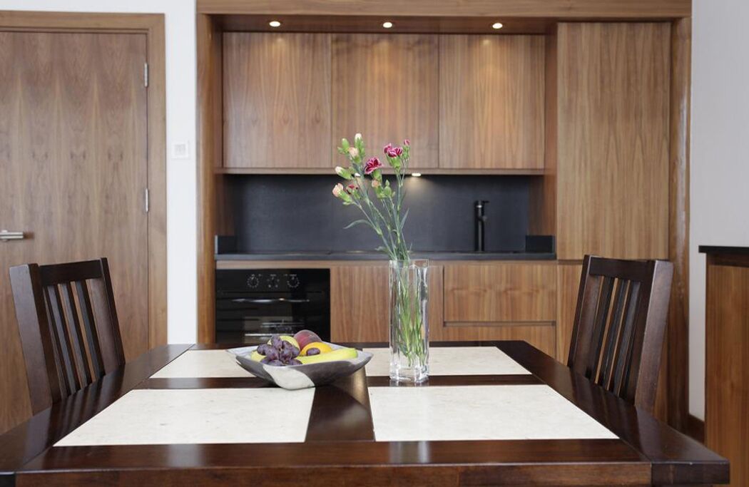A dining table with two chairs, a vase with flowers, and a fruit bowl.