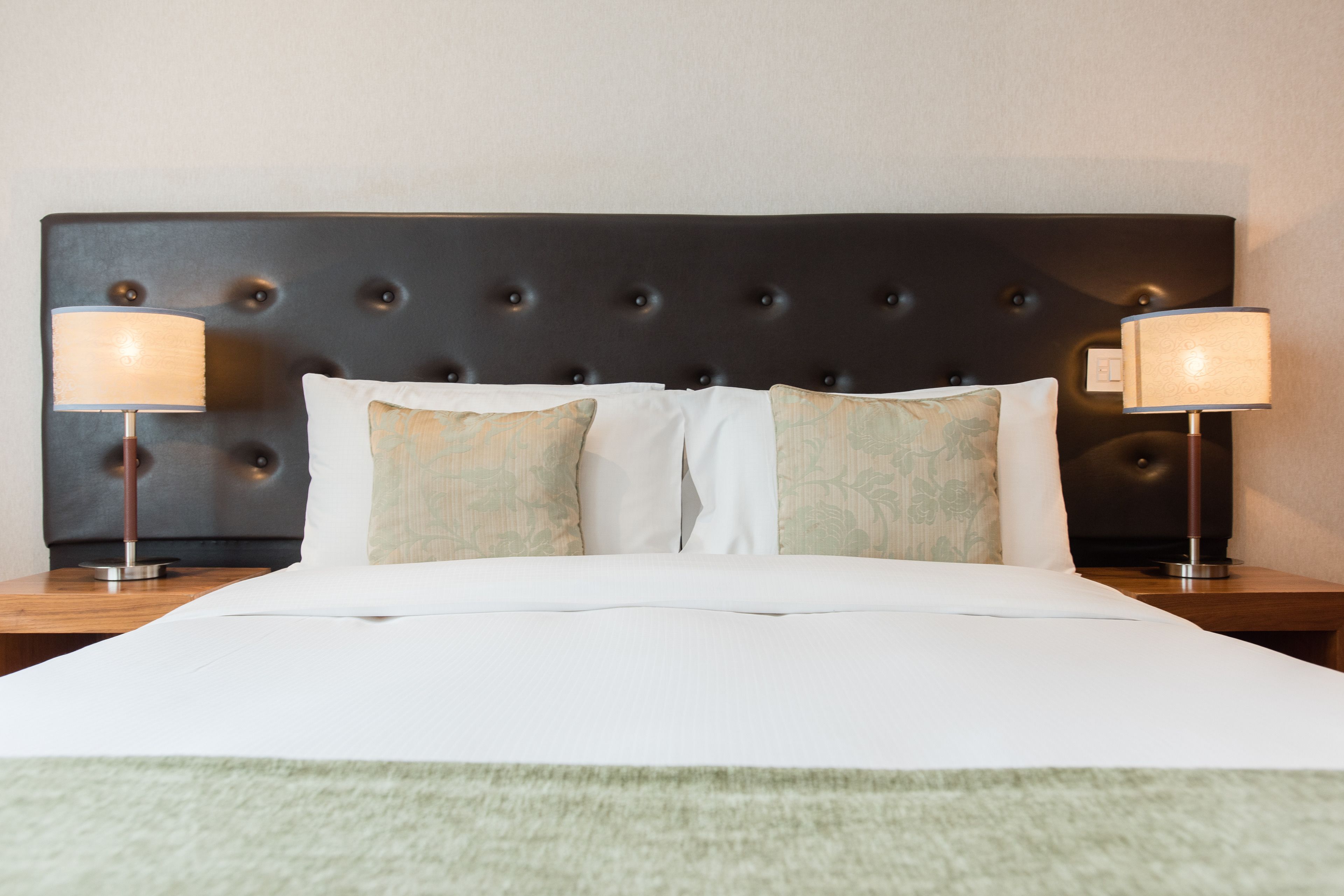 A neatly made bed with a tufted headboard, two bedside lamps, and a green throw blanket.