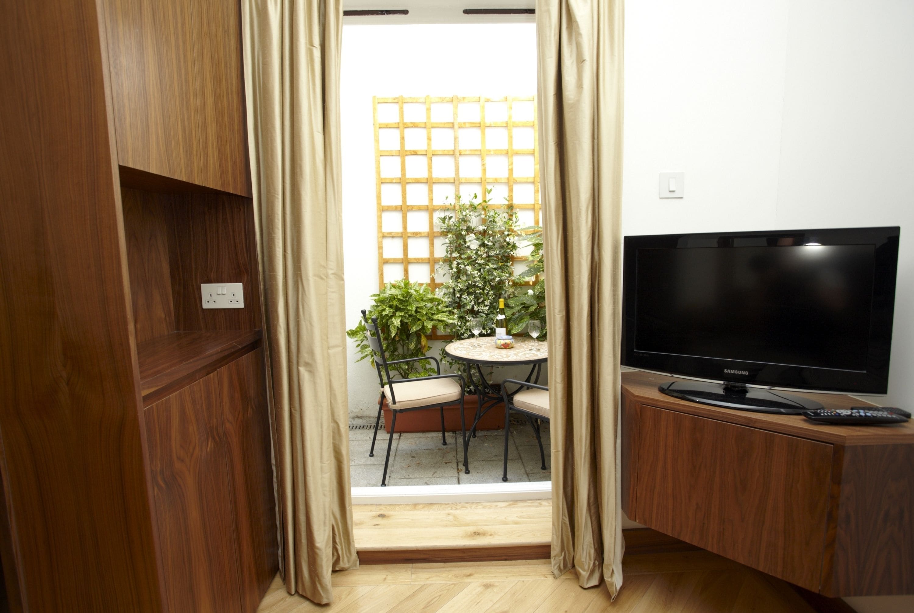Une pièce comprenant un meuble TV en bois, un téléviseur à écran plat, une table à manger avec des chaises, et une vue sur un jardin par la fenêtre.