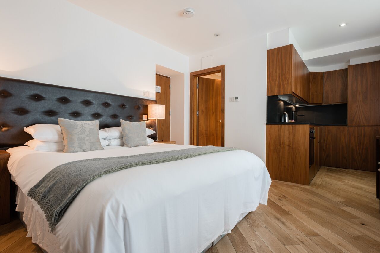 A bedroom with a large bed, a headboard, a bedside table, a lamp, and a wooden wardrobe.
