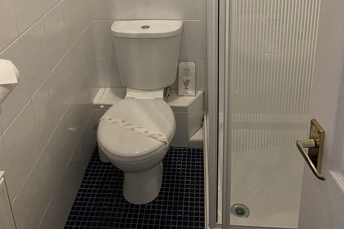 Um banheiro pequeno e moderno, com azulejos brancos, vaso sanitário, chuveiro com porta de vidro e piso revestido de azulejos pretos.