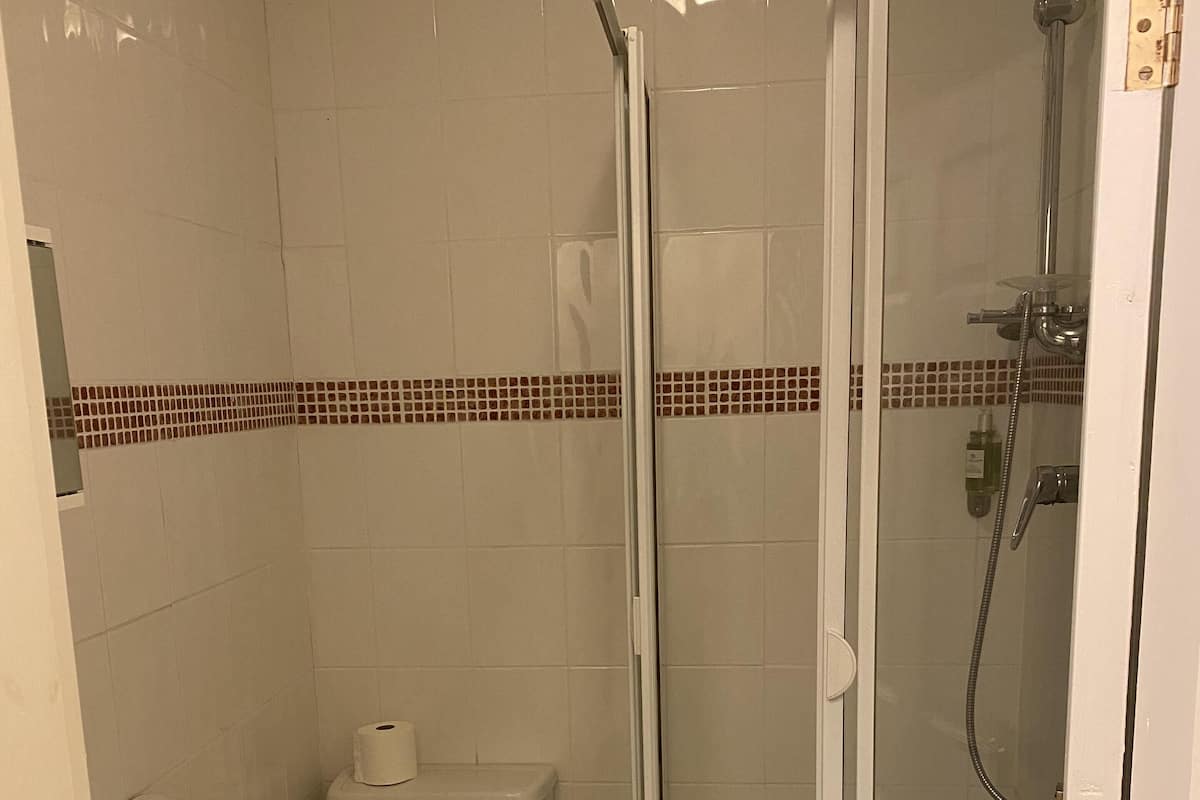 Casa de banho com sanita, lavatório e cabine de duche com portas de vidro.