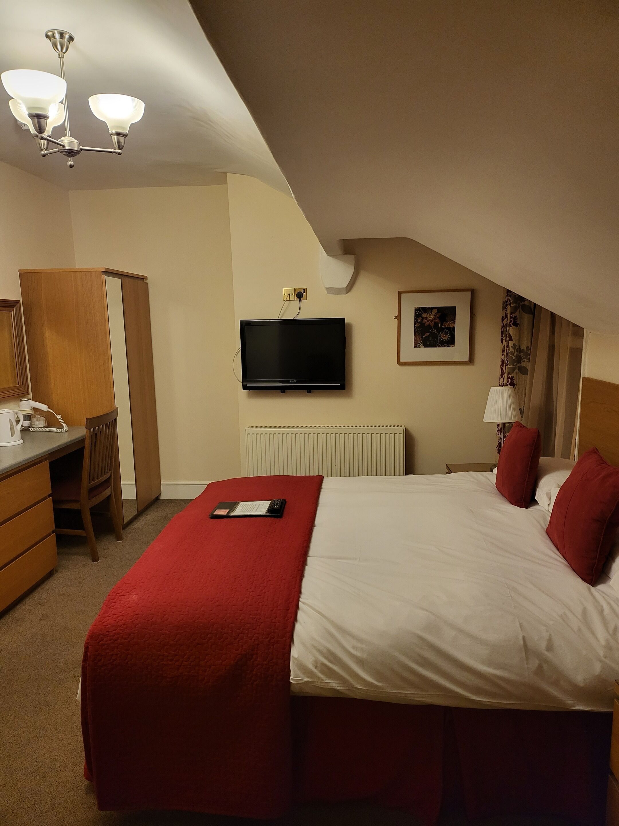 Ein Hotelzimmer mit einem Bett, einem Schreibtisch, einem Sessel, einem Fernseher und einer Heizung.
