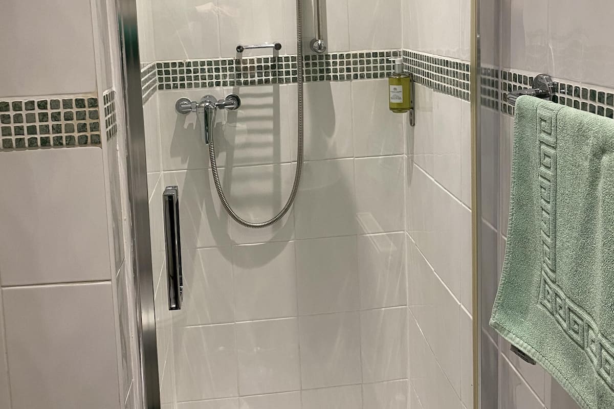 Um chuveiro com divisória de vidro, um chuveiro manual e uma torneira fixada na parede.