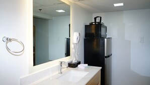 Un baño moderno con lavamanos, espejo, secador de pelo y un electrodoméstico negro en la pared.
