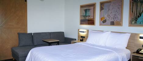 A hotel room with a bed, a sofa, a small table, and two wall-mounted lamps.