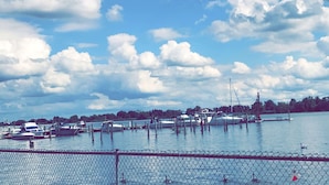 Un puerto deportivo con barcos amarrados, cielo despejado y una valla al frente.