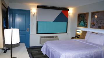 Habitación de hotel con cama, escritorio con lámpara, teléfono, calentador de pared y puerta.
