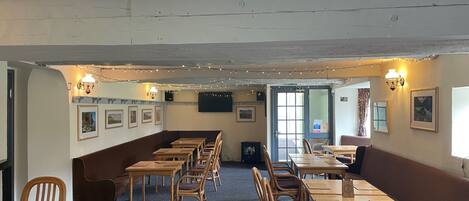 A restaurant with wooden tables and chairs, a long counter, and string lights on the ceiling.