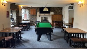 Um pub acolhedor com mesa de bilhar, mobiliário de madeira, paredes de pedra e uma televisão.