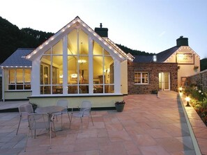 Una posada acogedora con un amplio ventanal de cristal, paredes de piedra y un patio con sillas.