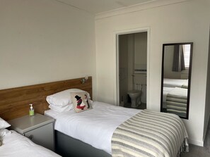 A hotel room with a wooden headboard, a single bed with white bedding, a bedside table with a bottle of hand sanitizer, and a mirror on the wall.
