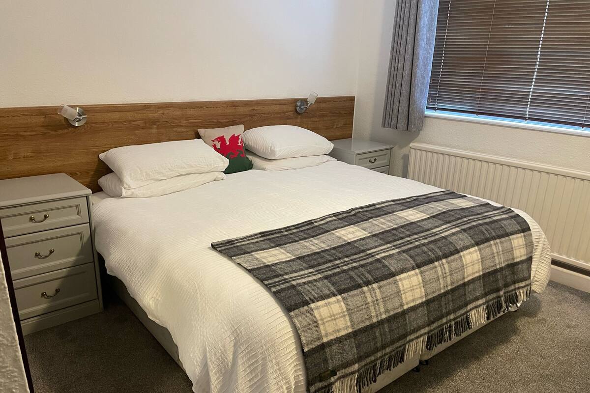 A neatly made bed with a plaid blanket, a wooden headboard, and a nightstand with drawers.
