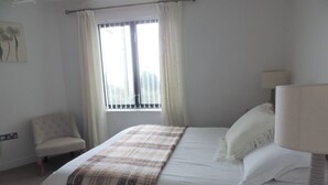 Quarto com cama, cadeira, mesa de cabeceira e janela com cortinas.