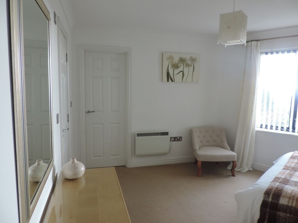 A bedroom with a bed, a chair, a white radiator, a door, and a wall-mounted artwork.