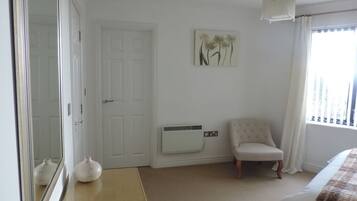 A bedroom with a bed, a chair, a white radiator, a door, and a wall-mounted artwork.