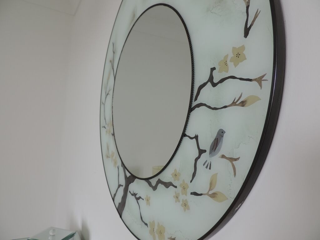 Un miroir rond fixé au mur, orné de motifs floraux et d’oiseaux.