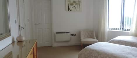 A bedroom with a bed, a chair, a dresser, and a radiator.