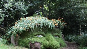 Escultura de jardim com rosto coberto de musgo e um chapéu de grama.