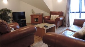 Uma sala de estar com sofás de couro marrom, uma televisão, uma mesa de centro e um armário.