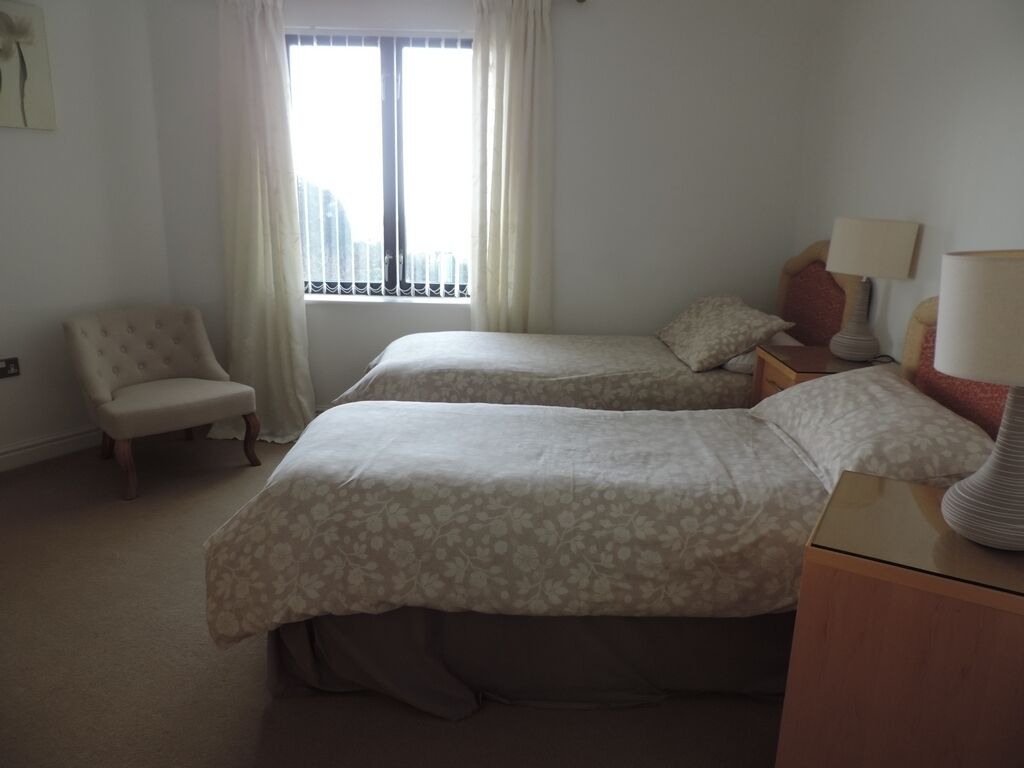 Camera da letto con due letti, una sedia, un comodino e una finestra con tende.