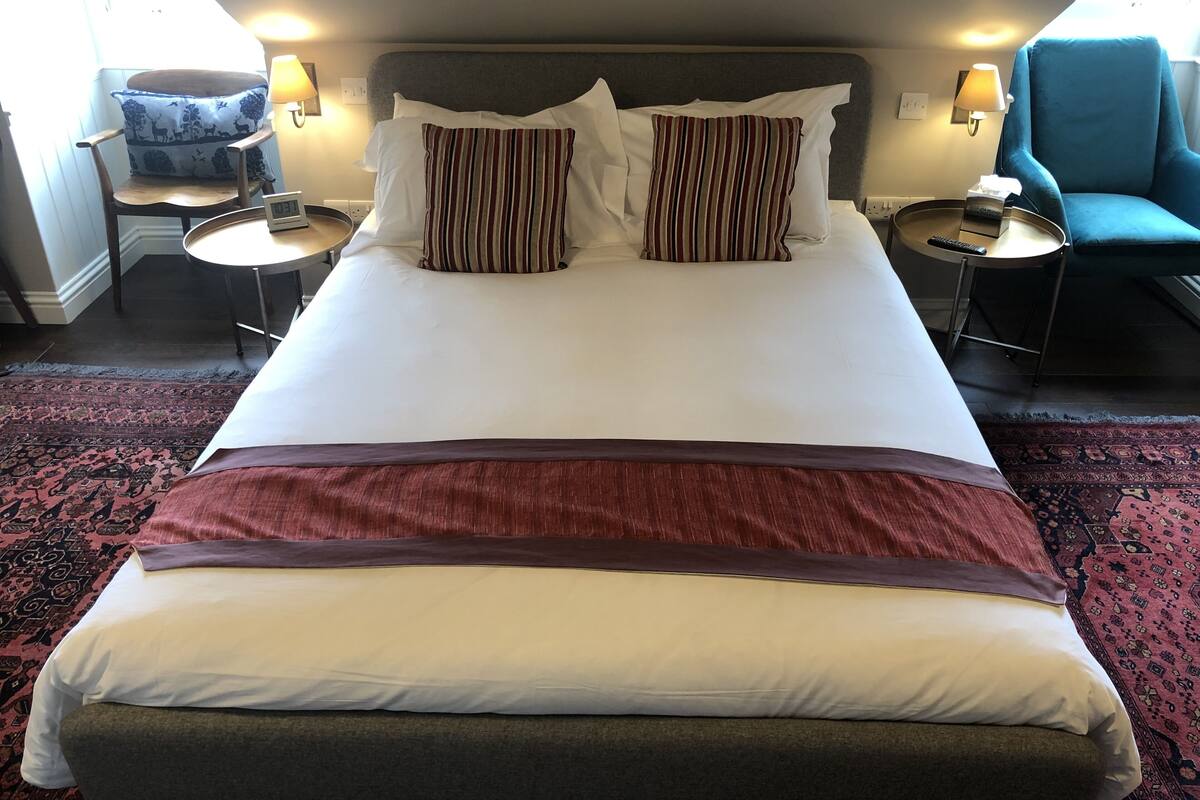 A hotel room with a large bed, two bedside tables, a chair, and a lamp.
