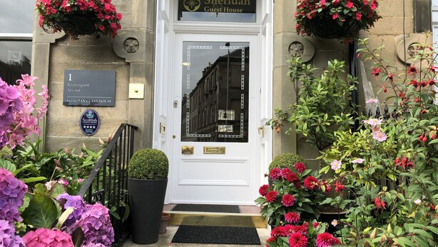 En hotelindgang med en hvid dør, et skilt der siger "Sheridan Guest House", og en plade der viser en pris fra Scottish Tourist Board.