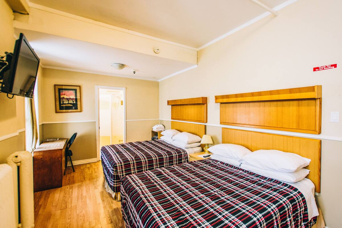 A hotel room with two beds, a desk, a chair, and a television.