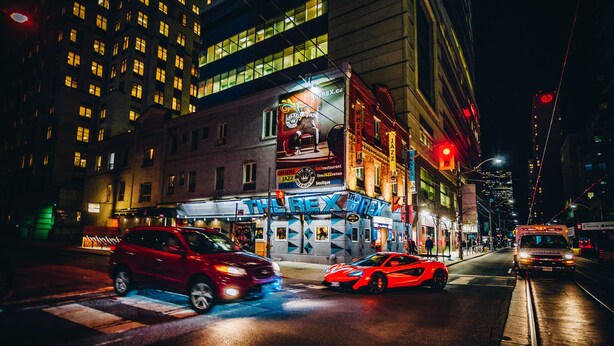 Una calle urbana iluminada en la noche, con un edificio que muestra un cartel grande para un restaurante y una boutique.