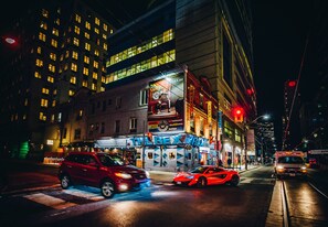 A brightly lit urban street at night with a building featuring a large sign for a restaurant and a boutique. - The Rex Hotel (Toronto)