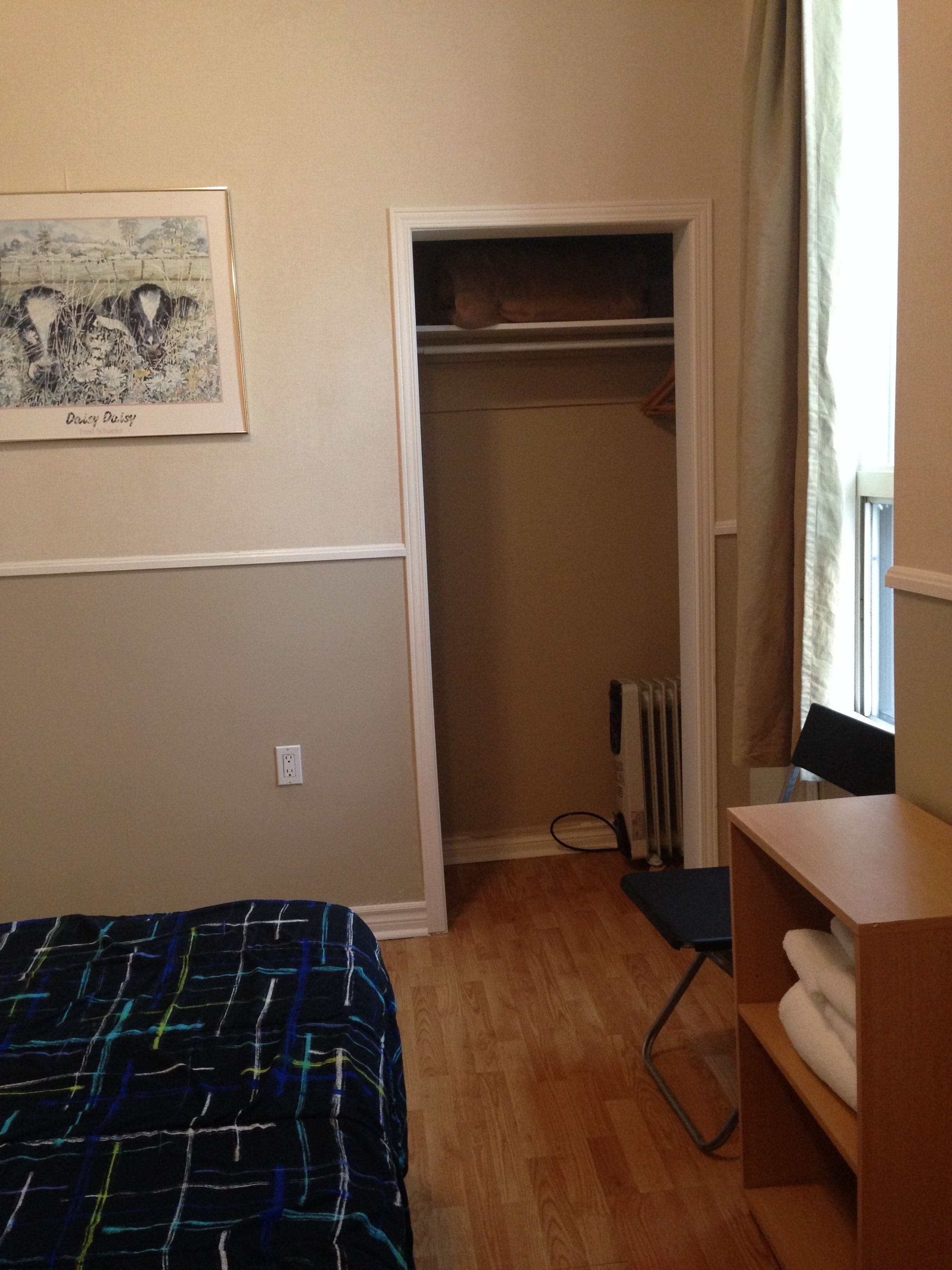 A bedroom with a bed, a desk, a chair, a radiator, and a closet.