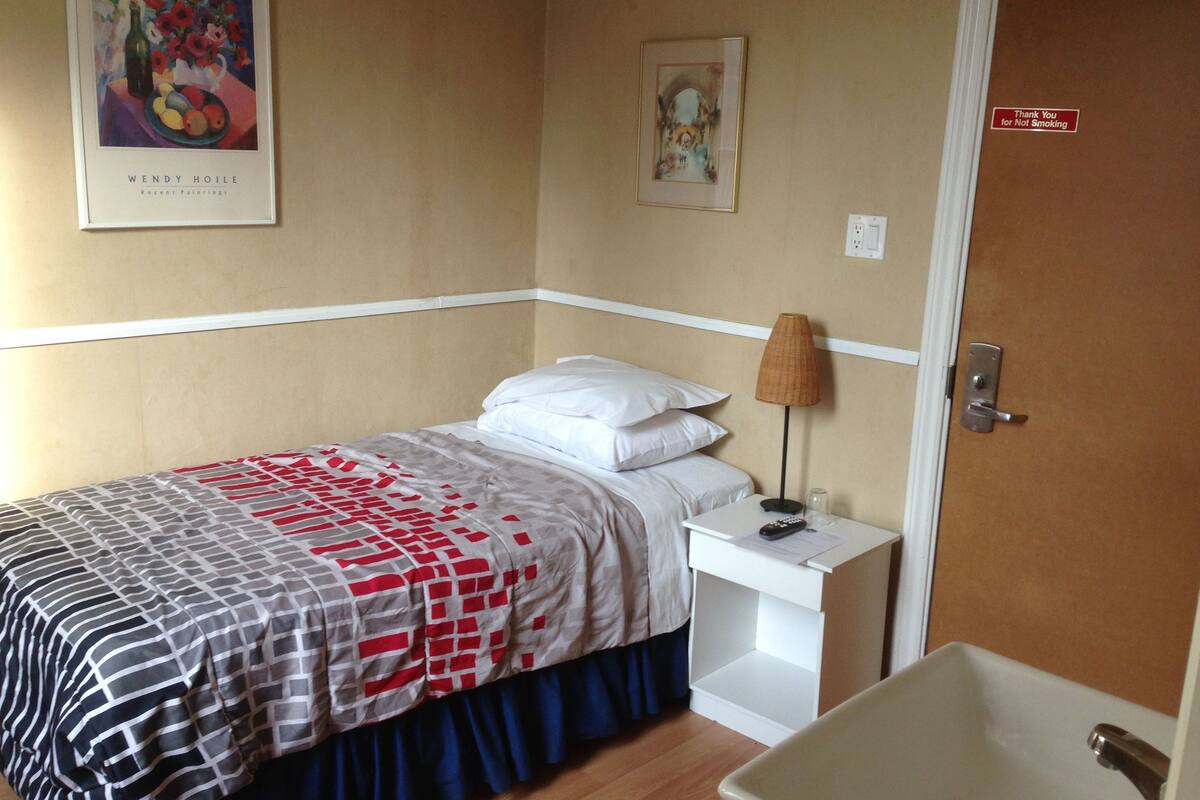 A hotel room with a bed, a nightstand, a lamp, a framed painting, and a bathroom with a sink.