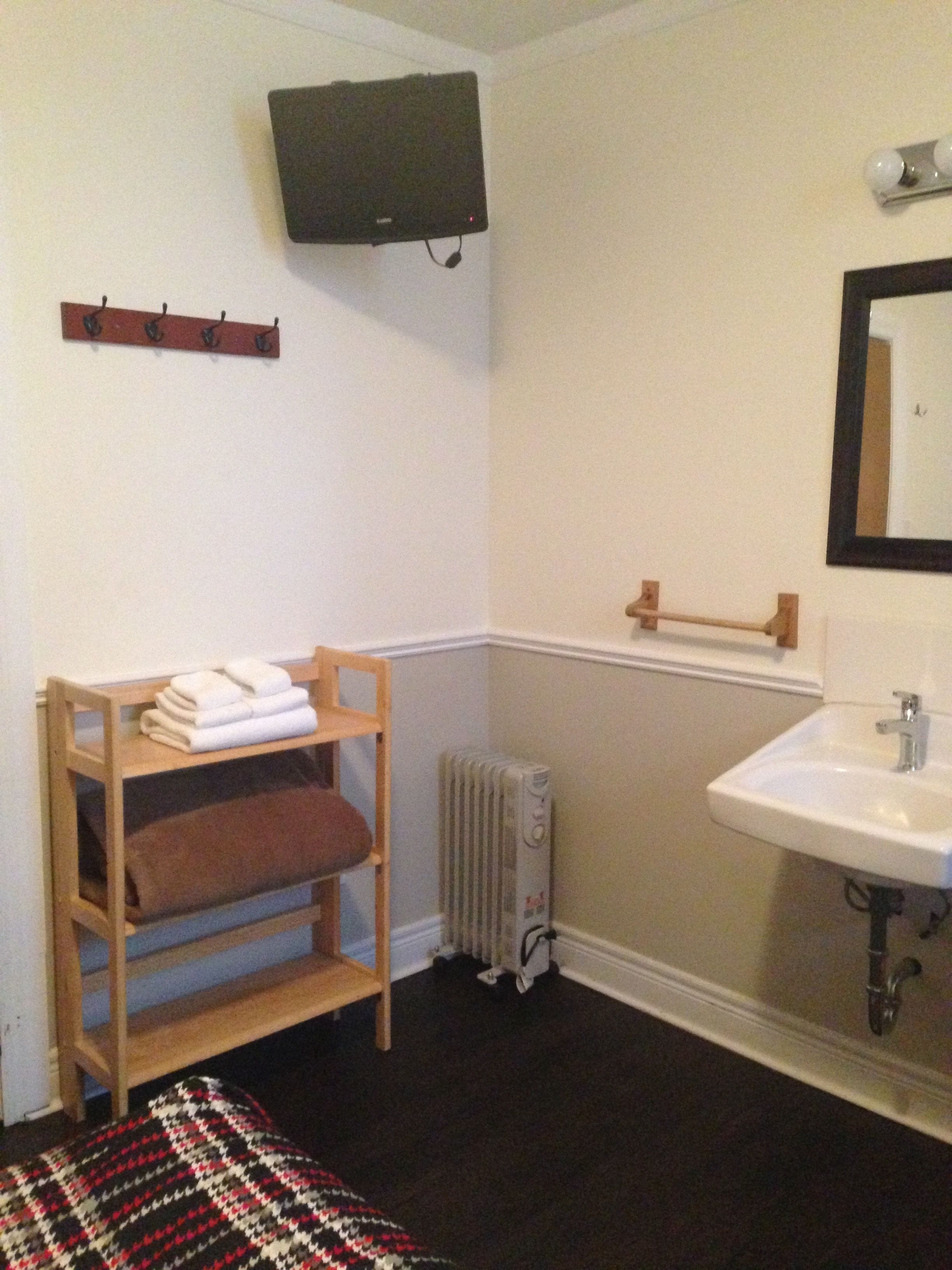 A bathroom with a wooden shelf holding towels, a radiator, a sink, and a television mounted on the wall.