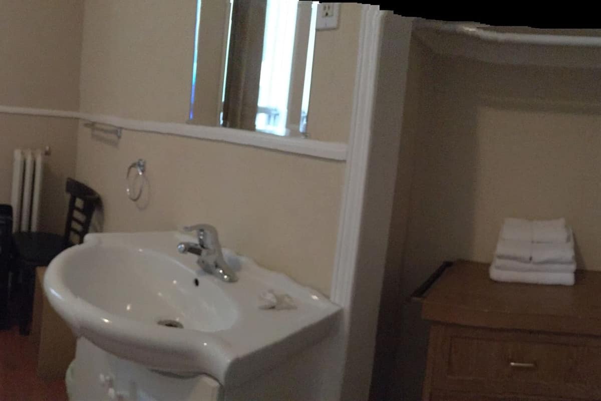 A small, compact room with two single beds, a white sink, and a mirror above it.