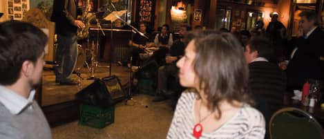 Un bar con una banda tocando, clientes sentados en mesas y un escenario con instrumentos musicales.