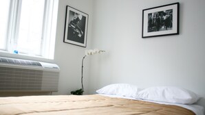 Un dormitorio con una cama, almohadas blancas, una orquídea blanca y dos fotografías blanco y negro en la pared.