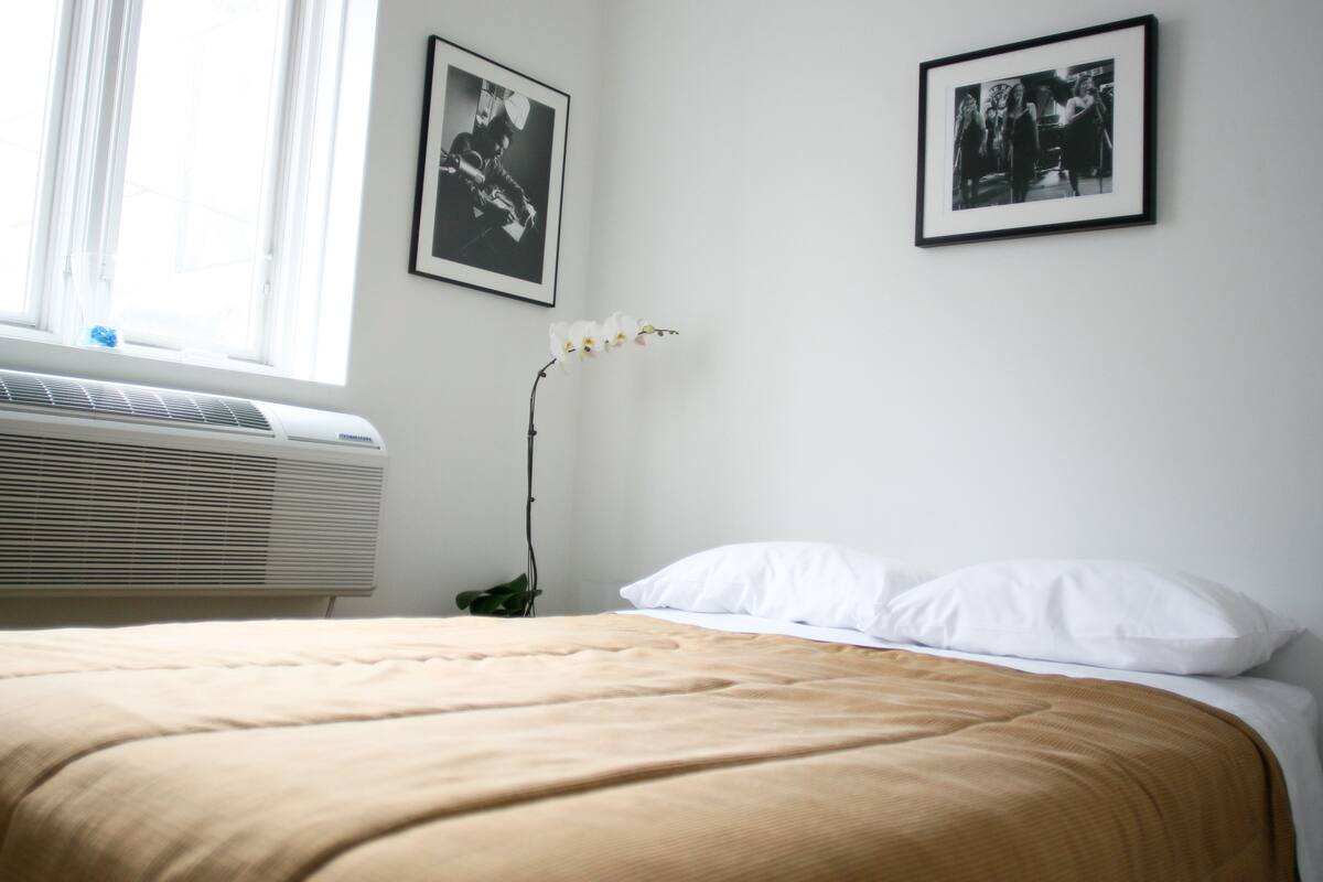 A bedroom with a bed, white pillows, a white orchid, and two black-and-white photographs on the wall.