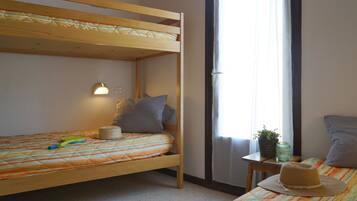 A bunk bed with a striped bedspread, a small bedside table with a plant and a candle, and a window with curtains.