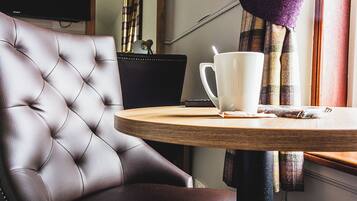 A tufted leather chair, a white mug, and a plaid curtain in a room with a television and a window.