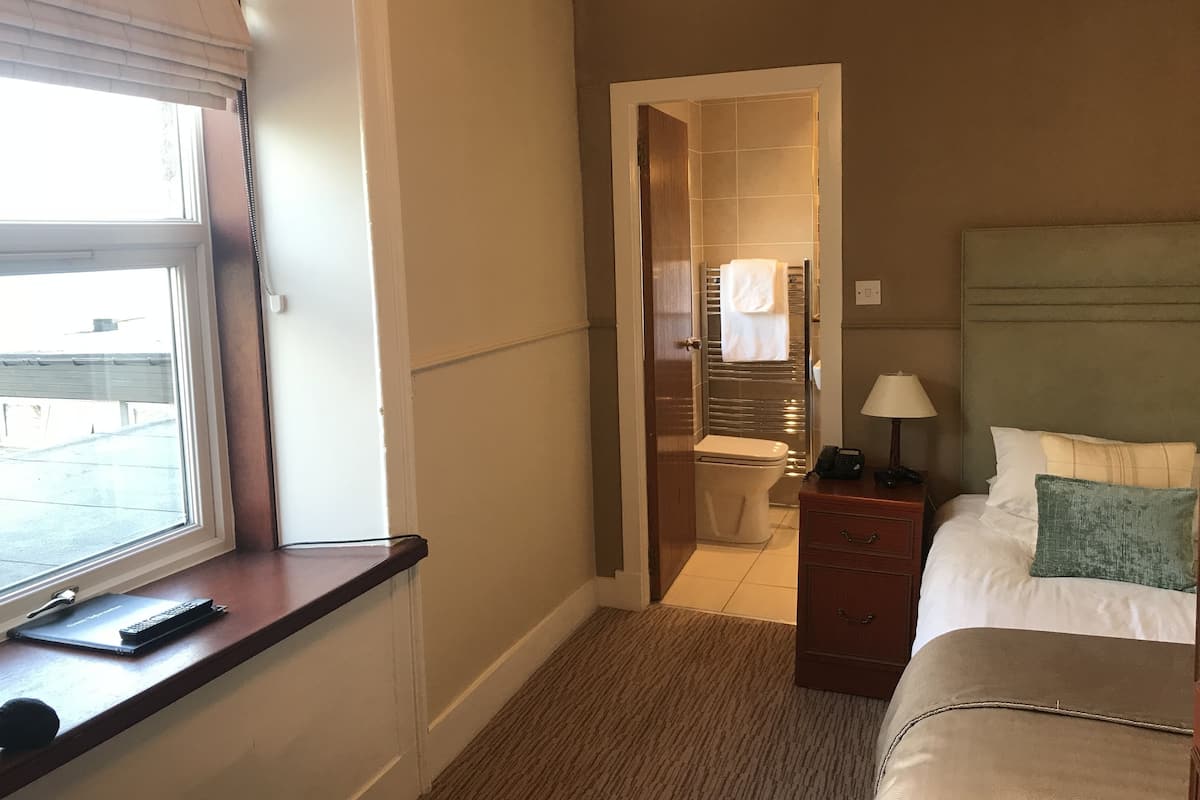 Una habitación de hotel con cama, mesita de noche, lámpara y vistas al exterior a través de una ventana.